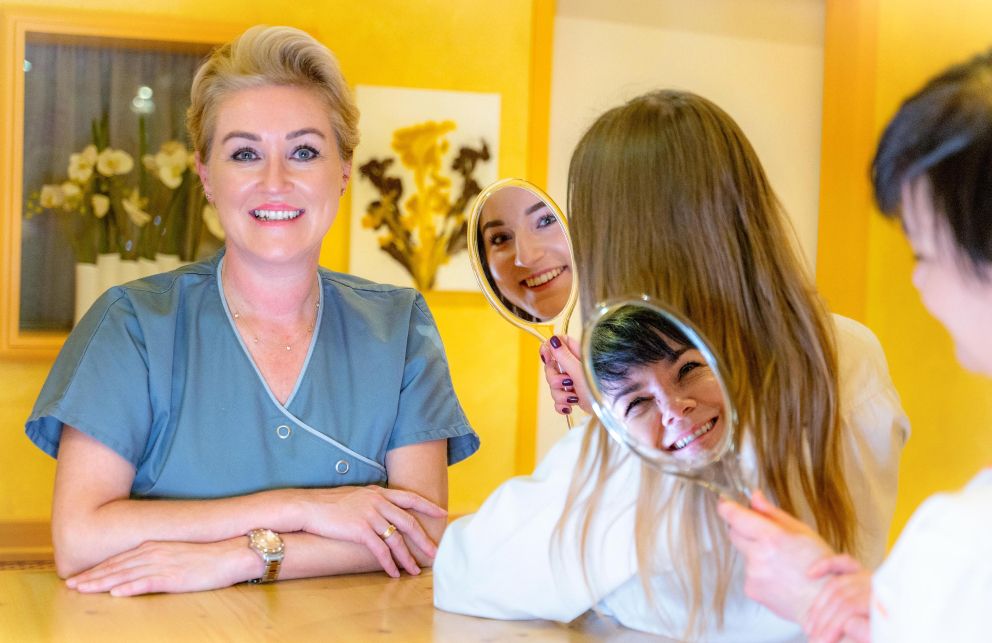 Drei Frauen, von denen zwei durch einen Spiegel schauen